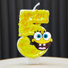 A yellow sponge cake candle shaped like the number 5, featuring a cartoon face.
