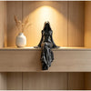 A black figurine of a hooded female figure stands on a wooden shelf with soft lighting.