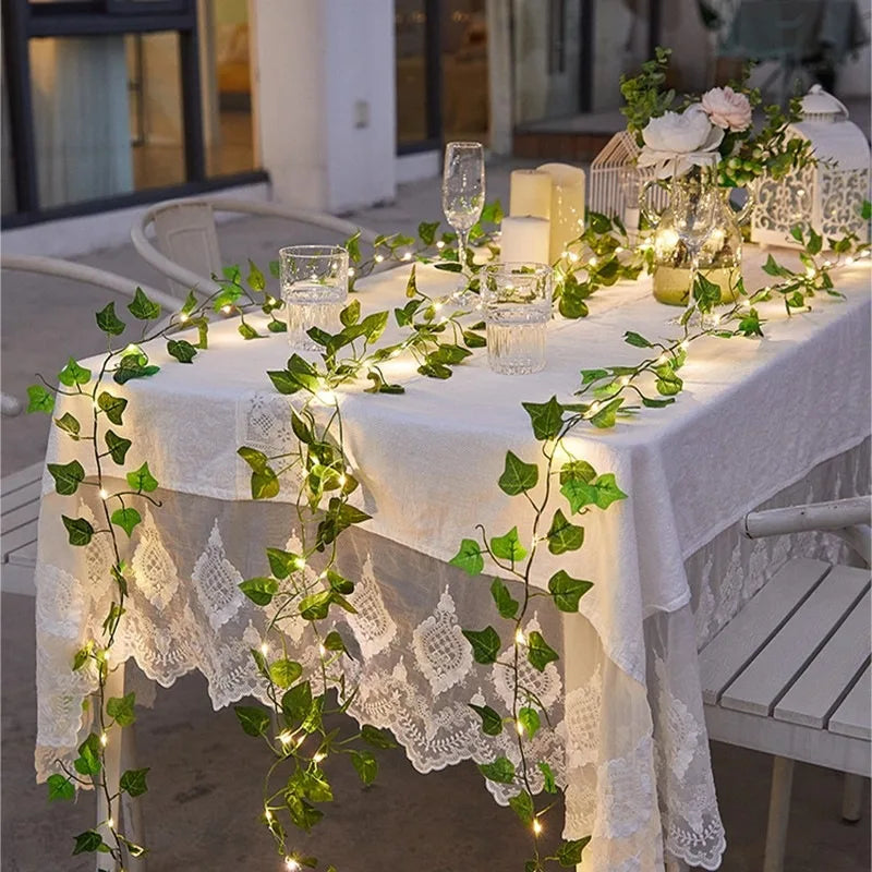 White lace tablecloth decorated with green leaf string lights and ivy vines for an outdoor or rustic setting.
