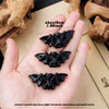 A hand holds three black natural obsidian bat figurines resting on a light background.