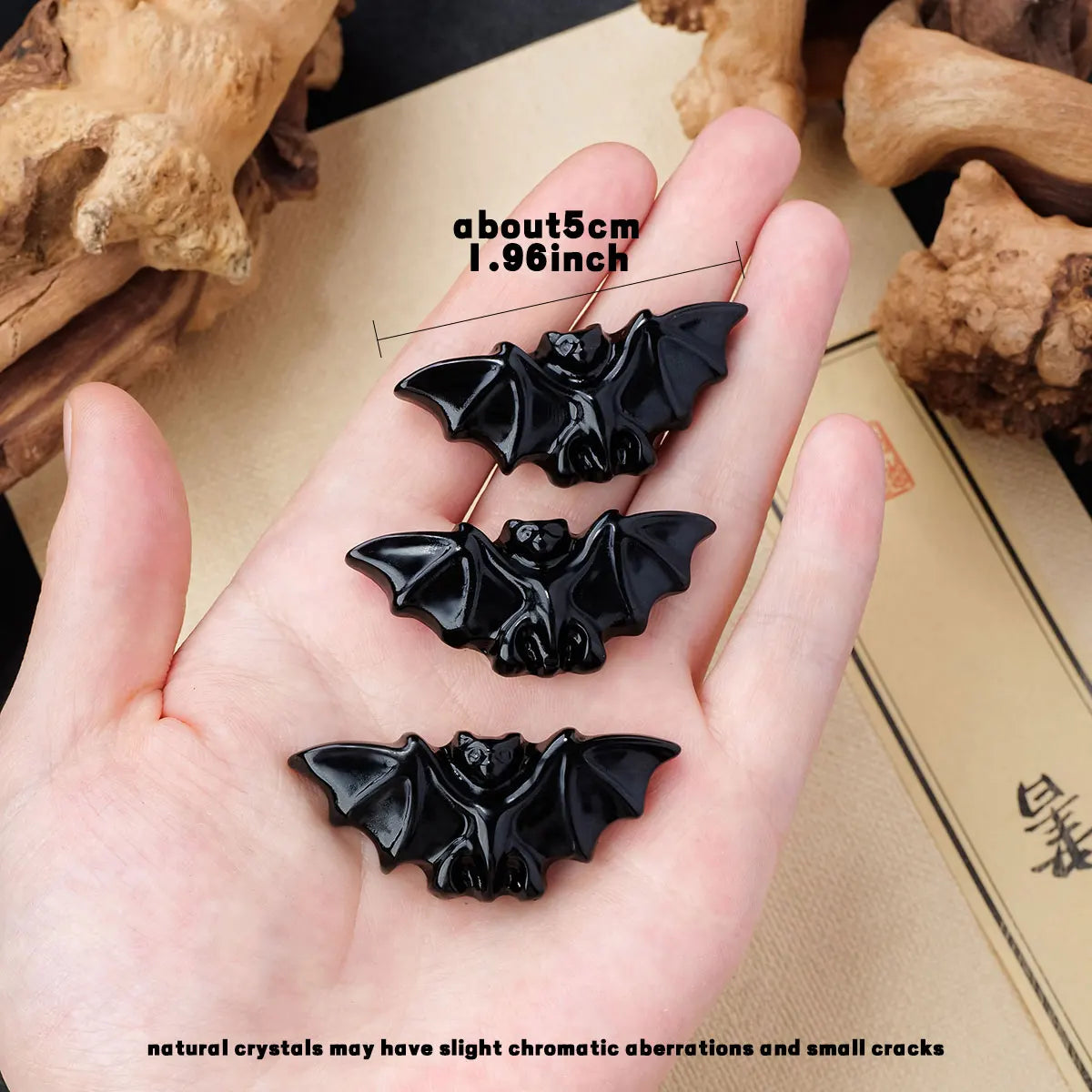 A hand holds three black natural obsidian bat figurines resting on a light background.
