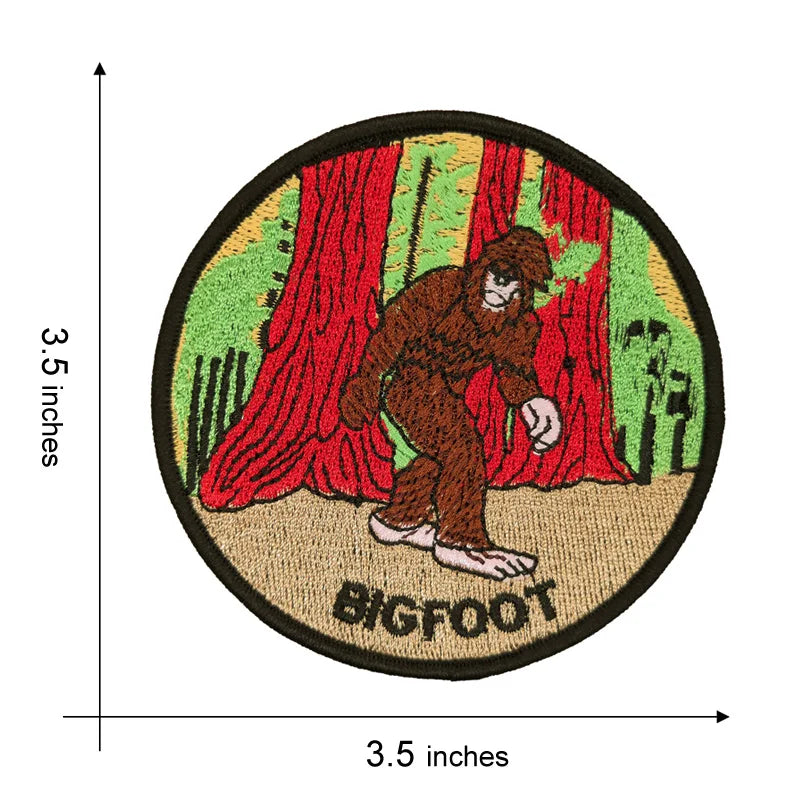 An embroidered patch featuring a brown Bigfoot figure standing in front of red curtains and green foliage.