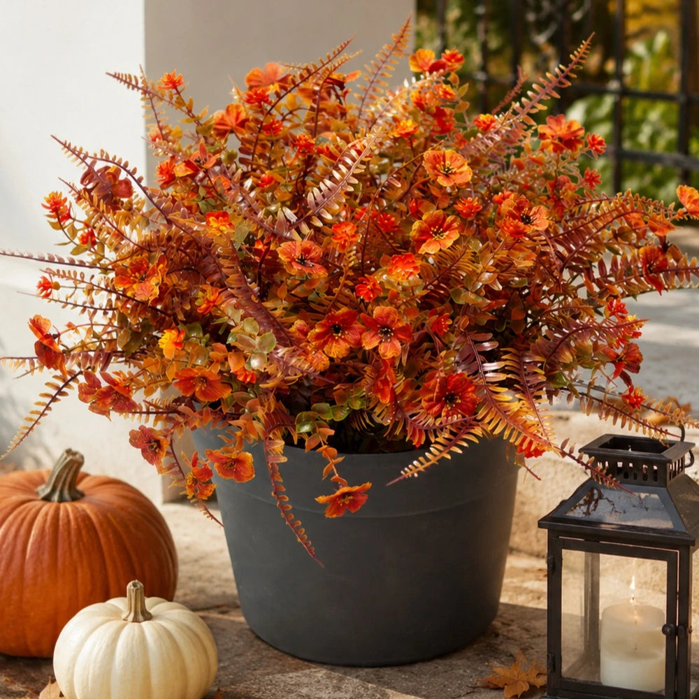 Topfpflanze mit künstlichen Herbstblumen in Orange- und Rosttönen auf Stein