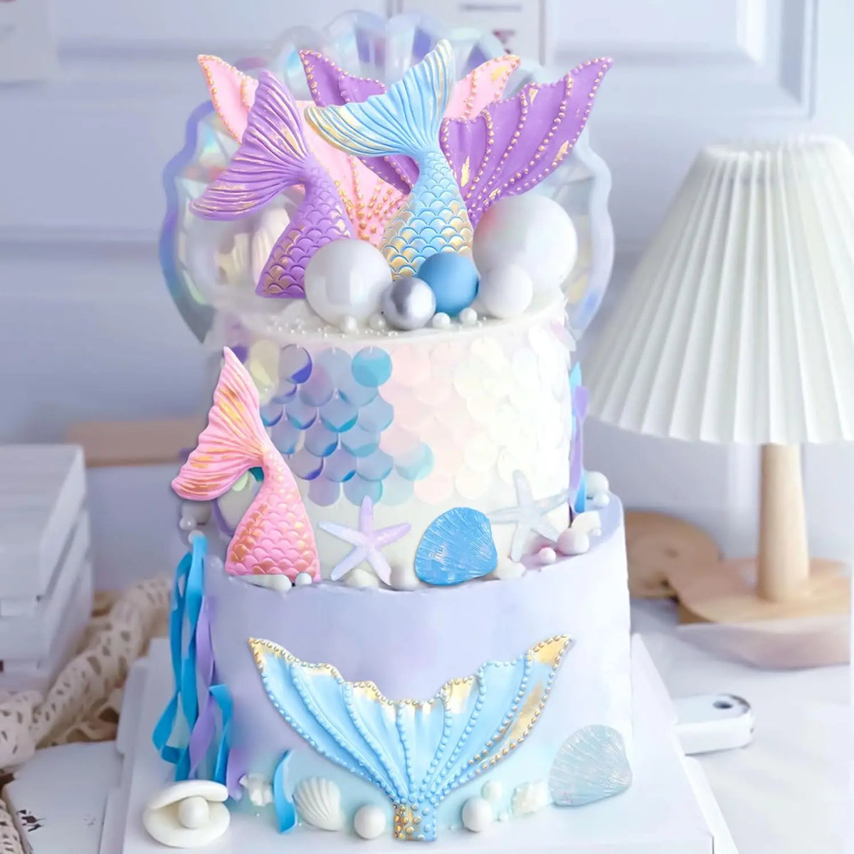 A tiered cake decorated with purple, blue, and pink mermaid tail shapes, seashells, and sea stars.
