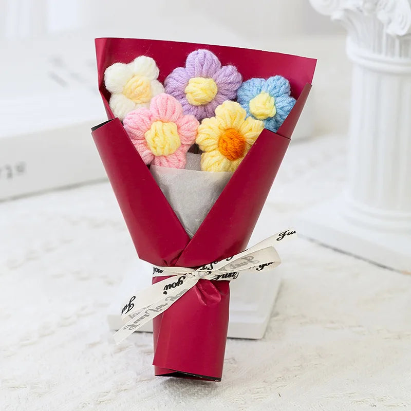 A bouquet of handmade crochet flowers in various pastel colors, including pink, yellow, and blue, wrapped in a deep magenta p