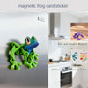 A green 3D frog fridge magnet with movable joints displayed on a silver refrigerator surface.