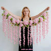A woman holds out her arms displaying a lush pink silk wisteria hanging vine garland.