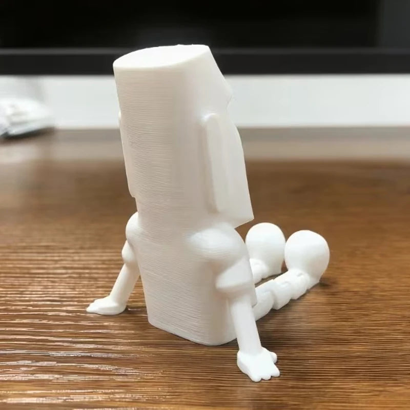 A white 3D printed Moai statue figurine with movable joints standing on a wooden surface.