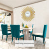 A modern minimalist metal wall clock with a sunburst design hangs on a white wall above a dining table.