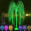 A large weeping willow tree light display with green LED strands illuminating a dark night scene.