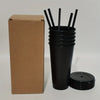 A black reusable tumbler is shown next to its cardboard packaging and several black straws and a lid.