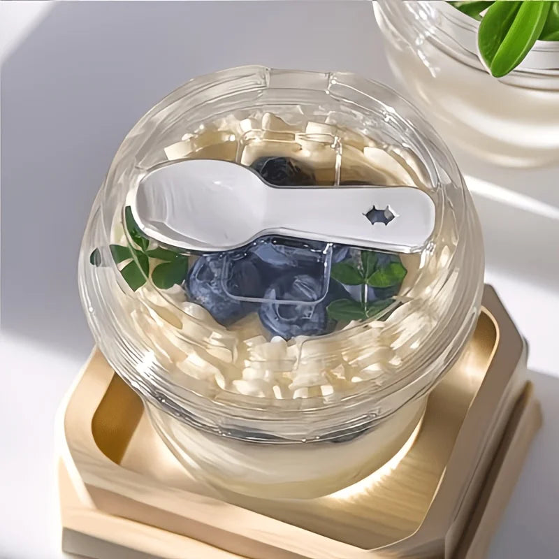 A clear dessert cup filled with creamy dessert topped with blueberries and a silver spoon, resting on a wooden tray.