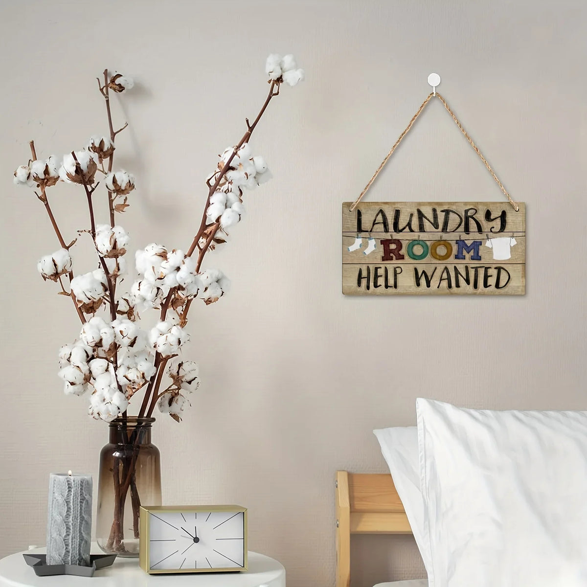 A vintage wooden farmhouse hanging sign with the text Laundry Room Help Wanted on a light gray wall.