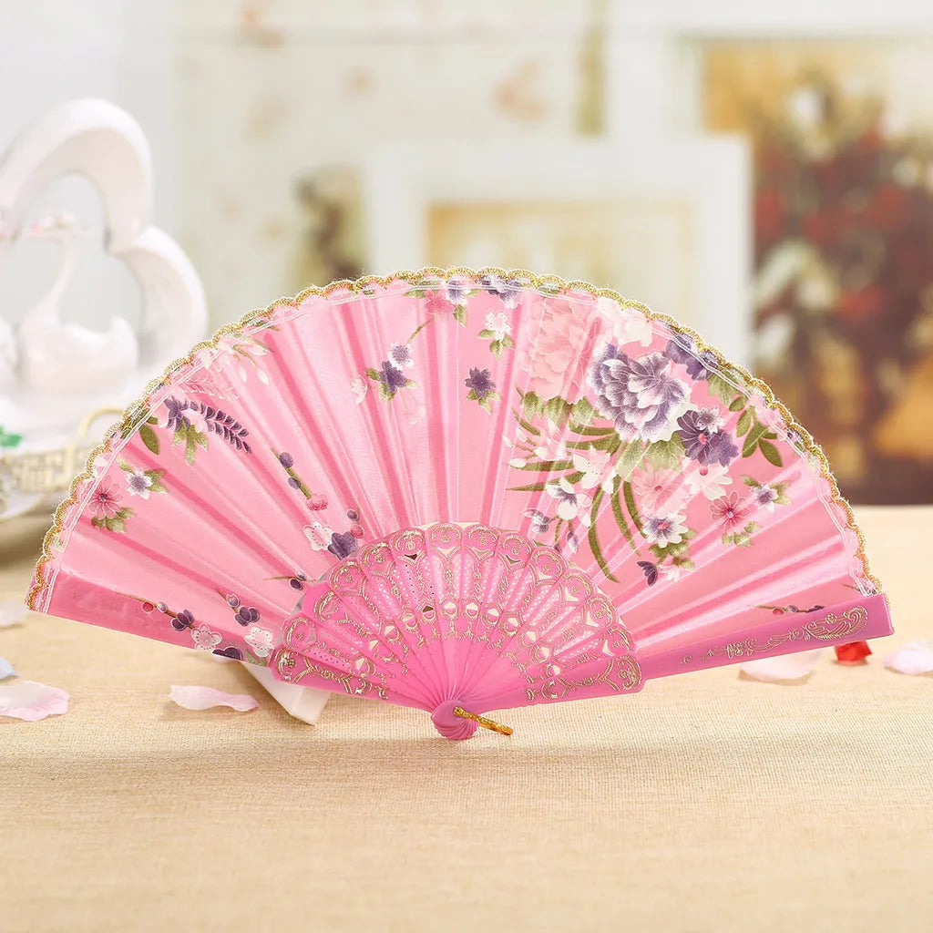 Pink vintage lace hand fan decorated with floral patterns resting on a wooden surface.
