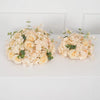 A bouquet of cream and pale yellow roses and hydrangea flowers arranged in a ball centerpiece.