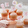 Pink cartoon bear cupcake toppers on sticks arranged around pink cupcakes for a baby shower or birthday party