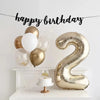 A large champagne gold foil number balloon shaped like the number 2 is displayed on a white shelf.