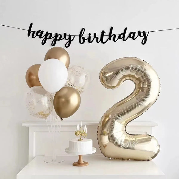 A large champagne gold foil number balloon shaped like the number 2 is displayed on a white shelf.