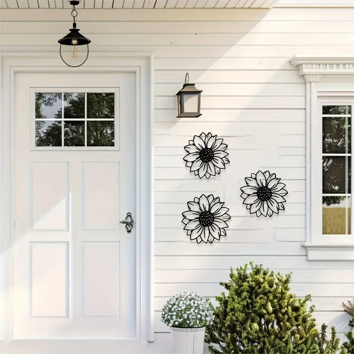 Black metal sunflower wall decor set mounted on white siding next to a white door and window