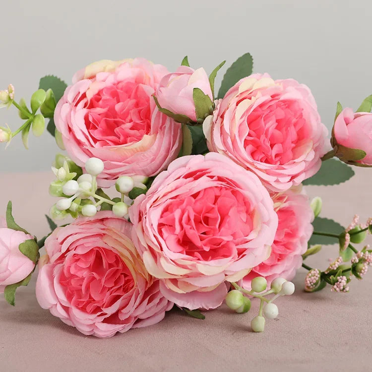 A bouquet of pink and peach silk rose and peony artificial flowers with green leaves.