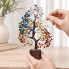 A hand holds a bendable crystal tree ornament featuring multicolored crystals and leaves.