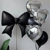 A collection of black and silver heart-shaped foil balloons, including a large bow and several hearts.