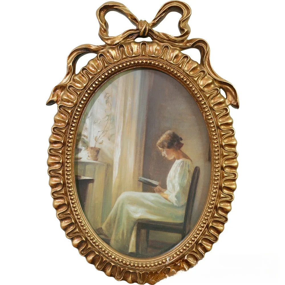 A vintage gold-toned bowknot picture frame with an oval frame, displaying a portrait of a woman.