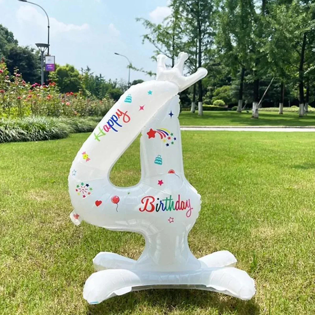 A white standing foil balloon shaped like the number 4 with a crown and birthday text, placed on green grass.