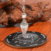 A crystal pendulum set featuring a clear quartz point mounted on an ornate silver chain and resting on a wooden divination bo