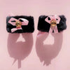 A black furry cat ear headband and tail costume set displayed against a pink background.