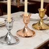 Three vintage iron candlesticks with ivory candles displayed on a marble table.