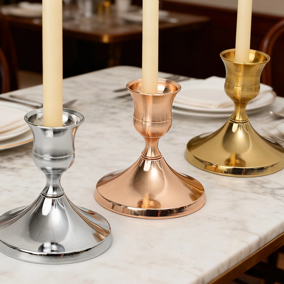 Three vintage iron candlesticks with ivory candles displayed on a marble table.