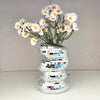 A bouquet of white and yellow daisy-like flowers displayed in a stack of silver mirror tile disco balls.