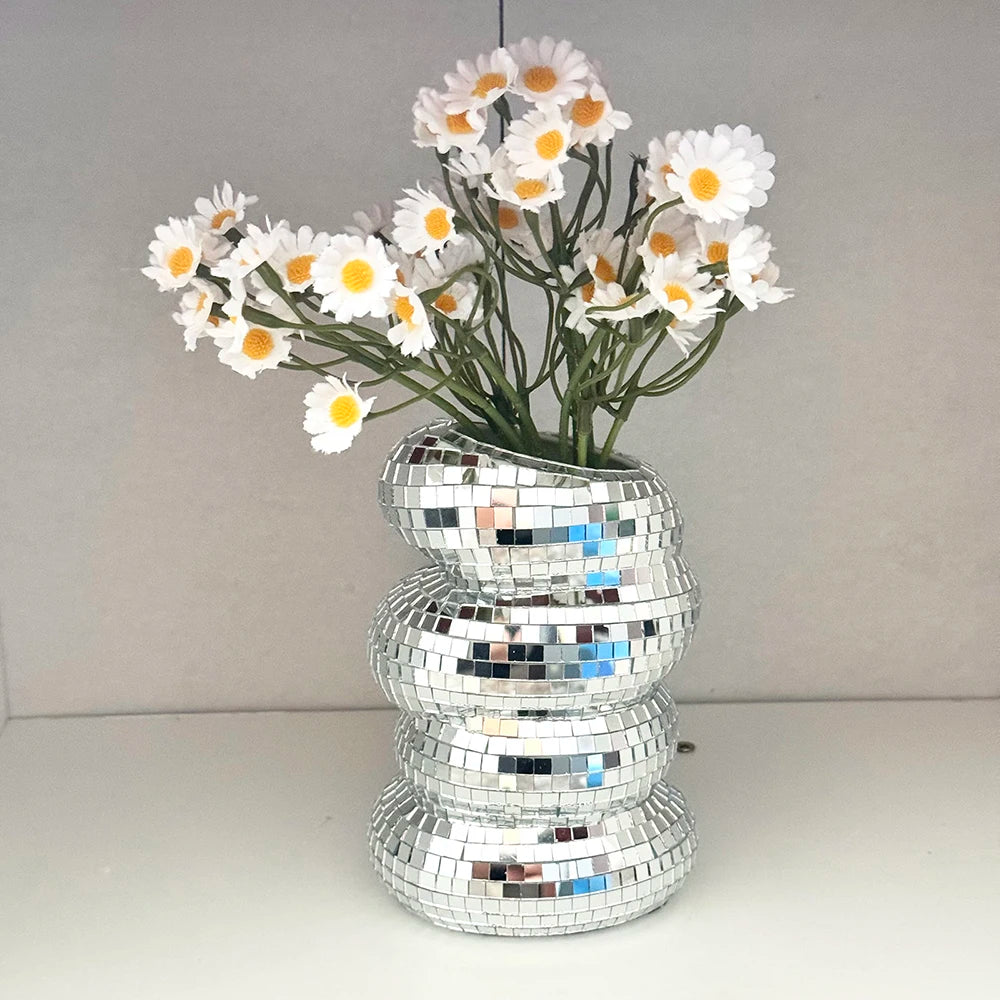 A bouquet of white and yellow daisy-like flowers displayed in a stack of silver mirror tile disco balls.