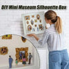 A woman is holding a framed silhouette box for a DIY mini museum project against a white brick wall.