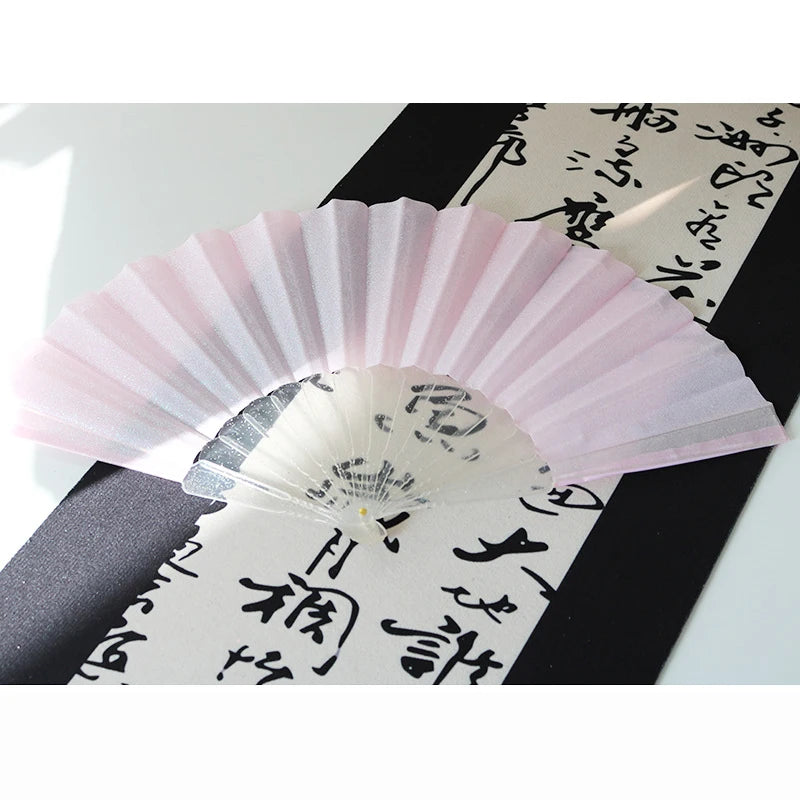 A pink glitter folding fan with transparent ribs is displayed against a dark background.