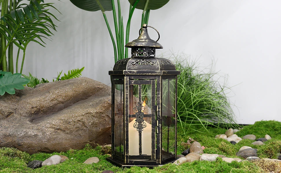A vintage Nordic iron candle lantern with glass panes sits on mossy ground next to large rocks and greenery.