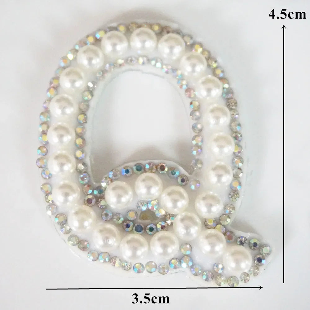 A white pearl letter Q rhinestone patch for clothing with iridescent accents.