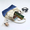A light beige canvas bag with blue accents holds a folding bamboo hand fan and sunglasses on a white background.