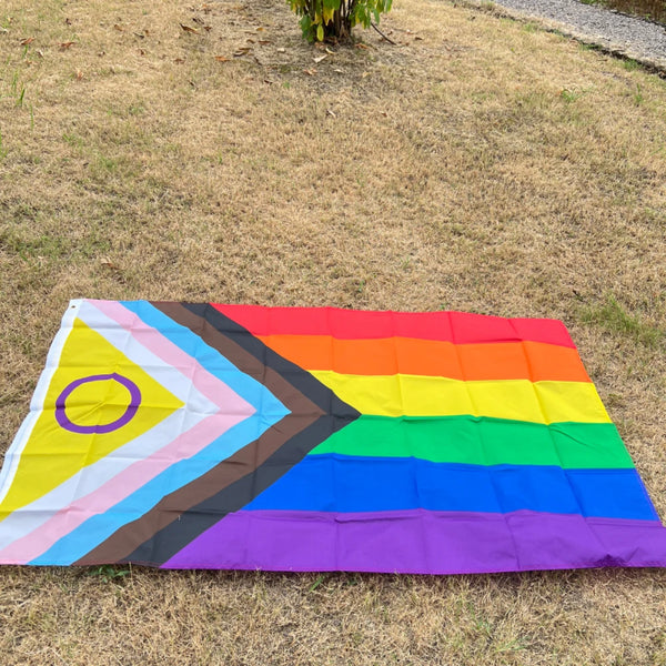 A horizontal Pride rainbow flag banner displayed on dry grass.