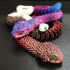Eine Sammlung bunter 3D gedruckter Schlangen-Fidget-Spielzeuge in verschiedenen Violett-, Pink- und Weißtönen.