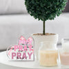 Pink acrylic heart sign with the text Pray on It Pray over it Pray through it displayed next to a candle and a green plant