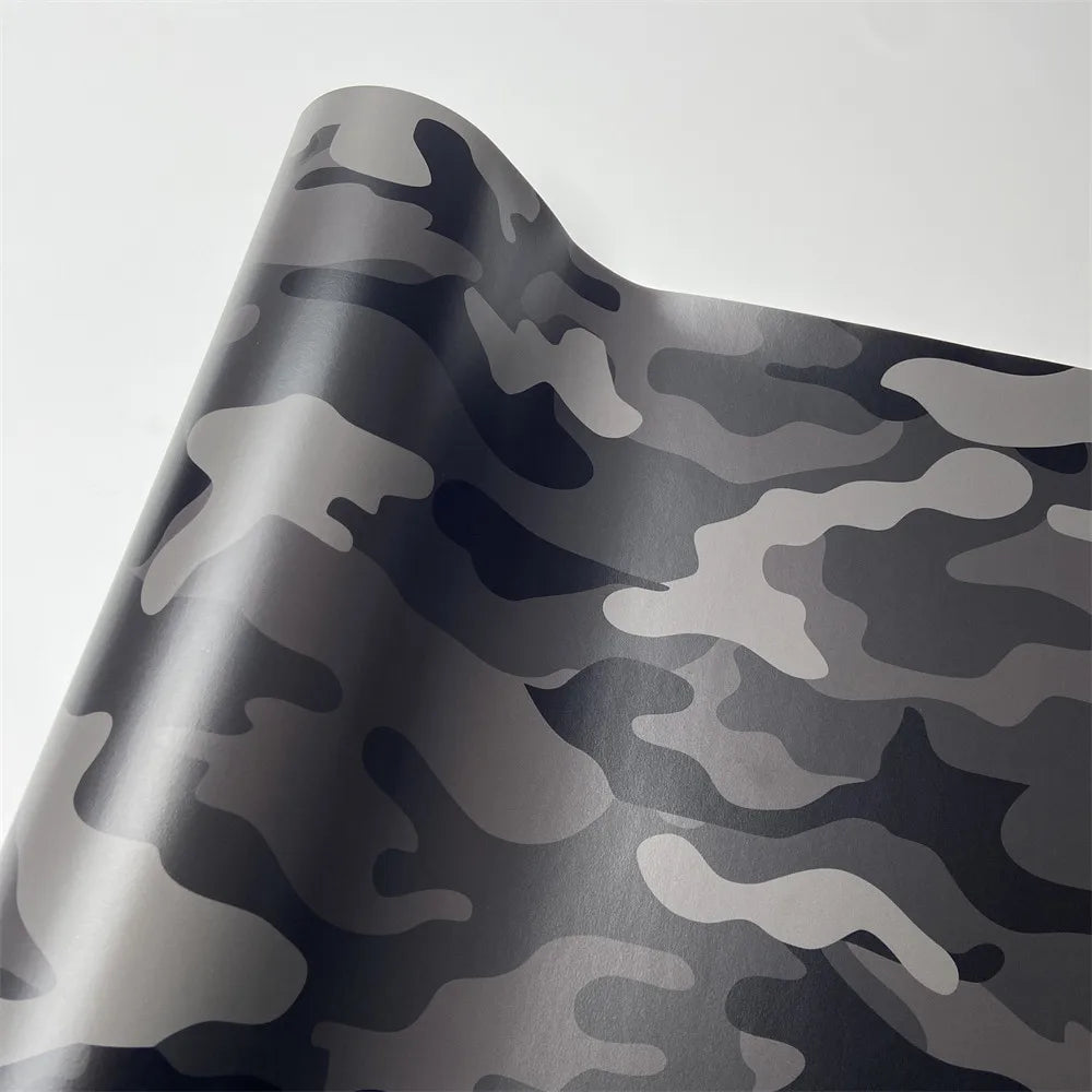A close-up of a gray and black digital camouflage vinyl wrap film rolled in a curved shape.