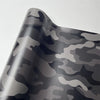 A close-up of a color-changing digital camouflage vinyl wrap film showing gray and black mottled patterns.
