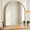 An arched full-length wall mirror with a gold frame resting on a wooden surface.