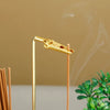 A gold-colored glass incense holder with a removable ash catcher is shown against a blurred background.