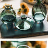 A set of three clear glass mini vases with a teal tint displayed on a dark book.