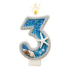 A glittery blue number three candle with a flame and seashells on a white background.