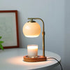 A brass aromatherapy wax melting lamp with a frosted glass shade and a lit candle on a white table.
