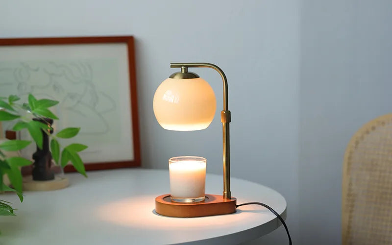 A brass aromatherapy wax melting lamp with a frosted glass shade and a lit candle on a white table.